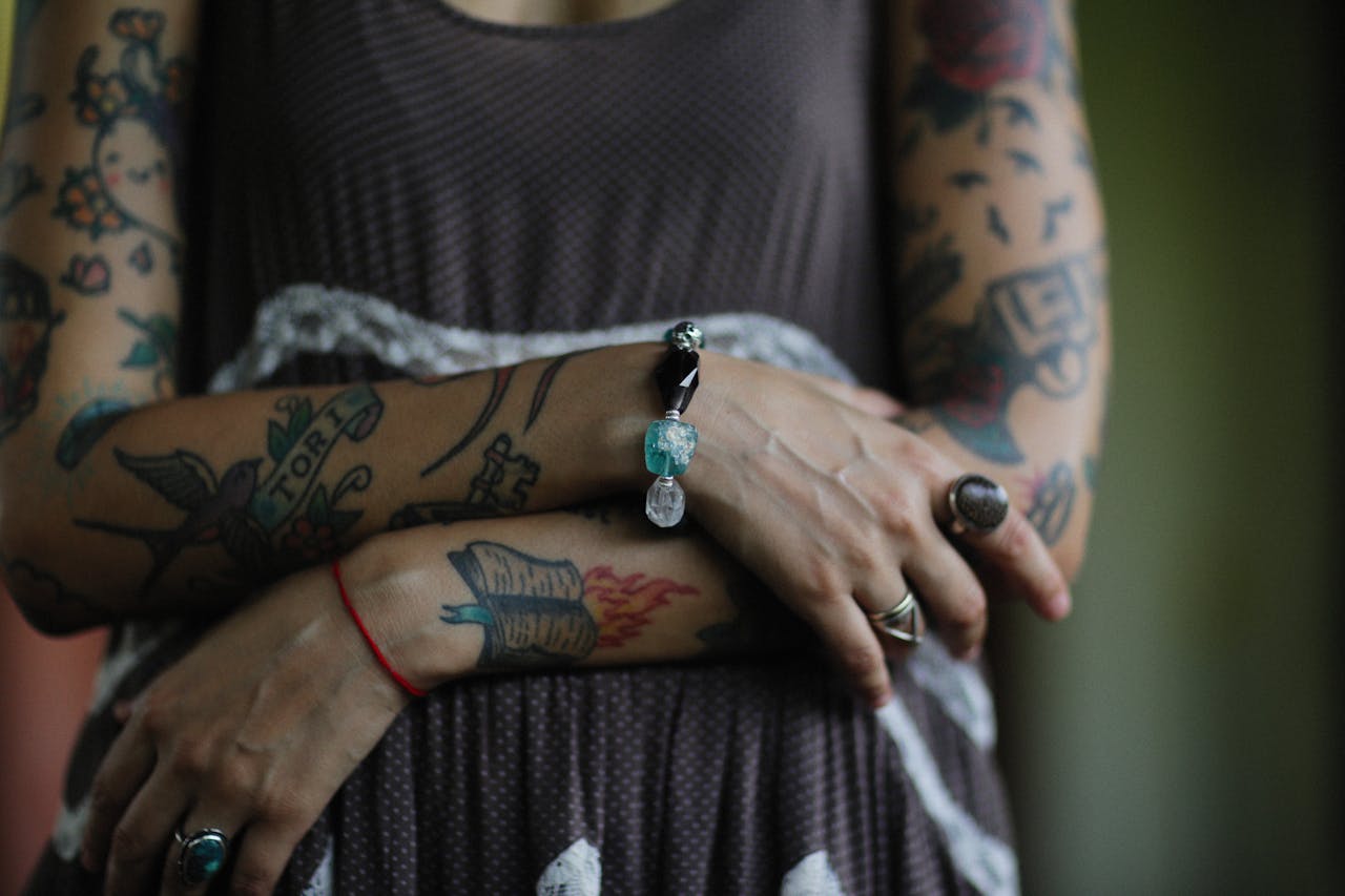 Close-up of tattooed arms adorned with rings and bracelet, showcasing body art and jewelry style.
