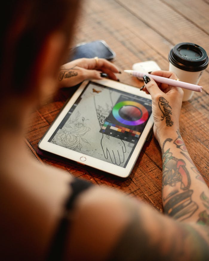 Tattooed artist using tablet and stylus for digital drawing. Coffee nearby.