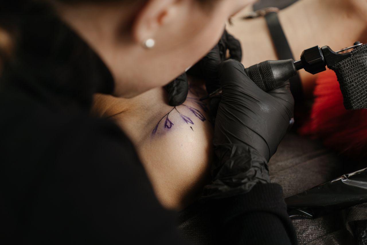 about-03 Close-up of a tattoo artist working on a client's arm with black gloves in a studio setting.