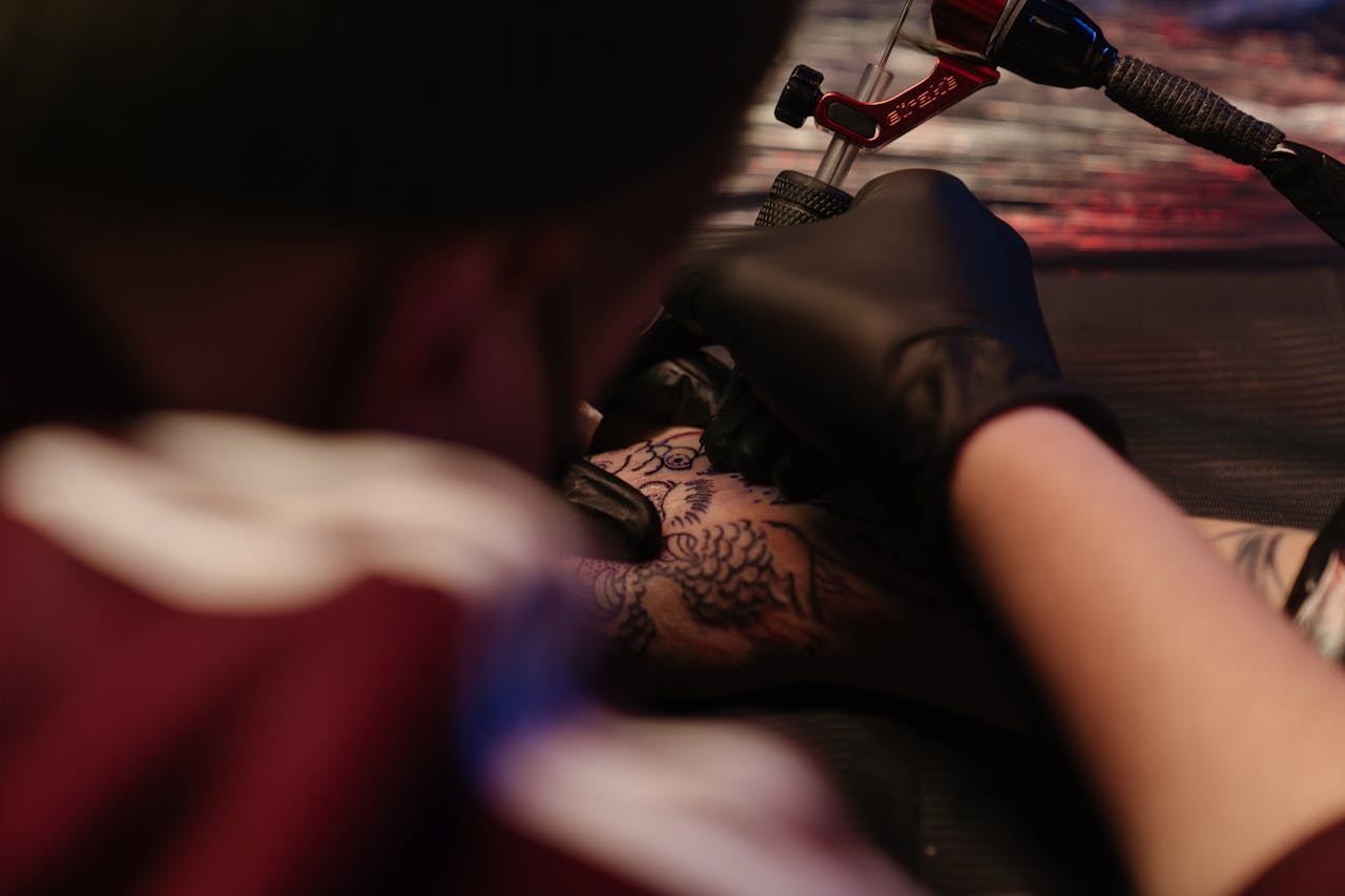 Tattoo artist using a machine to ink a design on a client's arm in a studio setting.